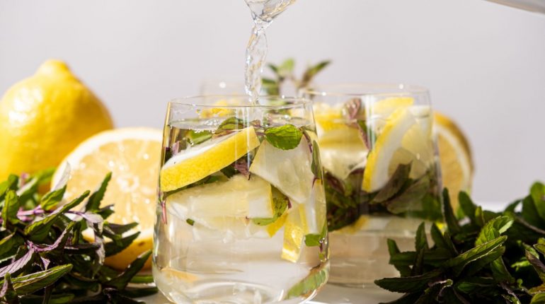 Zitronenwasser mit Minze wird in ein Glas gegossen, daneben frische Zitronen